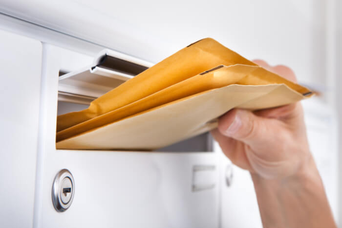 Person nimmt große Briefe aus Briefkasten