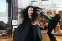 Frau mit abstehenden Haaren und Friseurin mit Laubbläser